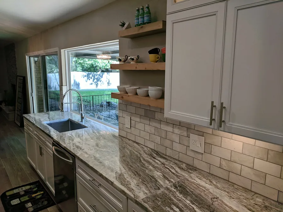 Light cabinetry and textured backsplash tile around a sink.