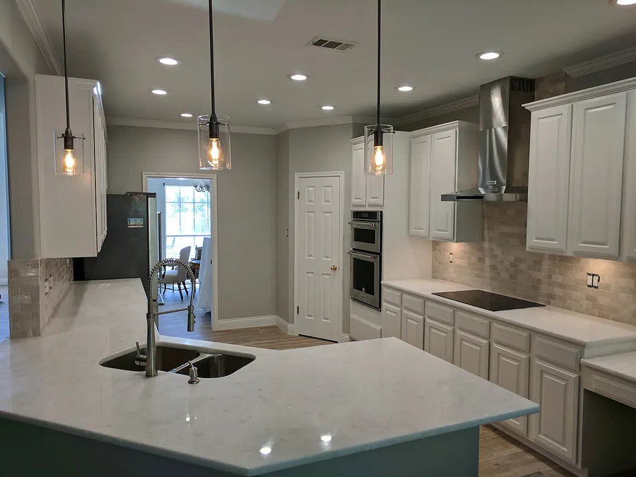 Bright kitchen with white cabinets, polished island and decorative pendant lights