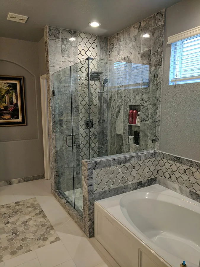 An updated bath featuring stone-look tile and glass shower panels.